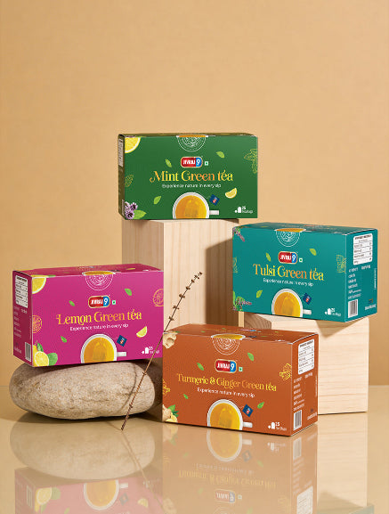 Four boxes of different flavors of green tea on a reflective surface with a beige background